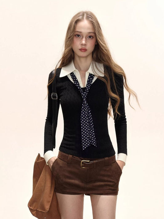 Woman wearing a black fitted knit sweater with a white collared shirt underneath and a navy polka dot tie, paired with brown shorts.