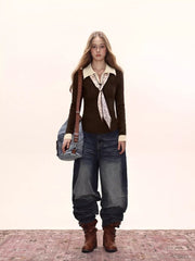 Full body shot of a woman wearing a dark brown fitted knit sweater with a cream collared shirt underneath and a patterned tie, paired with dark wash wide-leg jeans and brown boots.