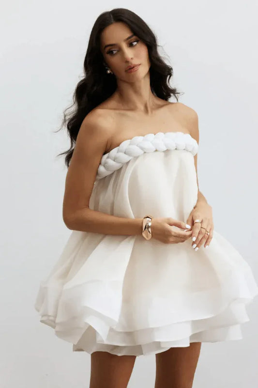 Woman wearing a white strapless mini dress with a braided rope detail at the bust and a layered, voluminous skirt.
