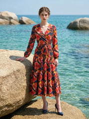 Woman wearing a long-sleeved floral print midi wrap dress with a tiered skirt, posing on a rocky beach with the ocean in the background.