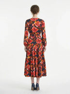 Back view of a woman wearing a long-sleeved floral print midi wrap dress with a tiered skirt, standing against a white background.