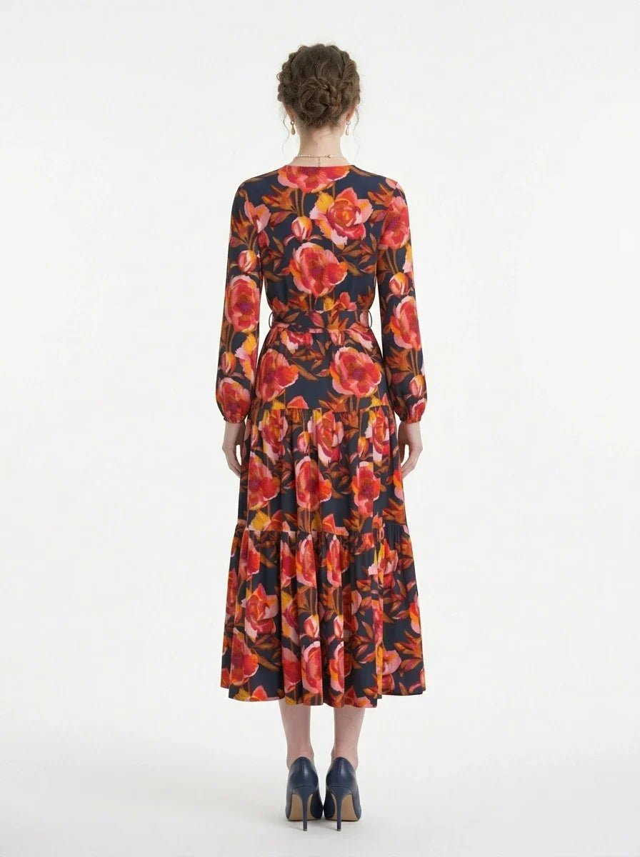 Back view of a woman wearing a long-sleeved floral print midi wrap dress with a tiered skirt, standing against a white background.