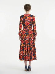 Back view of a woman wearing a long-sleeved floral print midi wrap dress with a tiered skirt, standing against a white background.