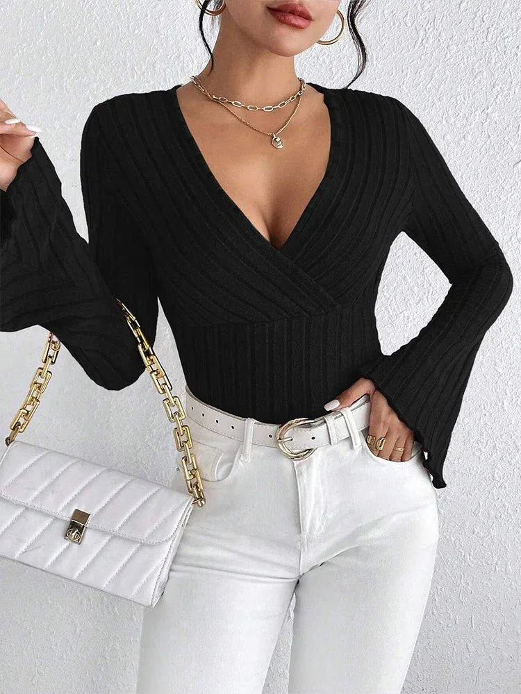 Woman holding a white quilted handbag and wearing a black long-sleeved ribbed knit top with a plunging V-neckline and flared sleeves, paired with white pants and gold jewelry. Secondary image