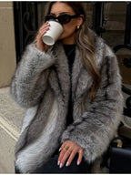 Woman wearing a grey faux fur coat, black top, black jeans, black boots, sunglasses, and gold earrings, holding a coffee cup.