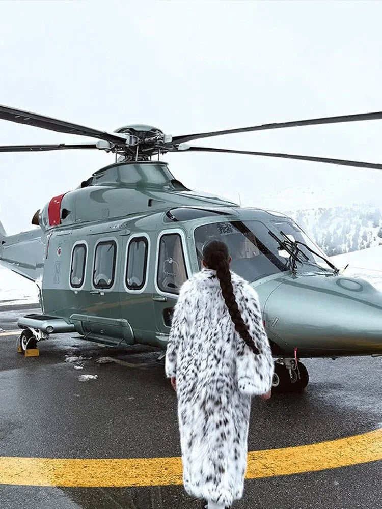 Woman in a long white and black spotted faux fur coat standing in front of a helicopter.