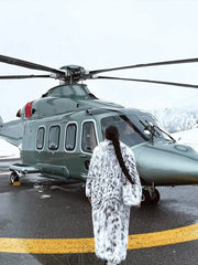 Woman in a long white and black spotted faux fur coat standing in front of a helicopter.