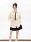 Woman wearing an oversized beige striped button-down shirt with a brown tie and a black pleated skirt, white socks, and brown loafers.