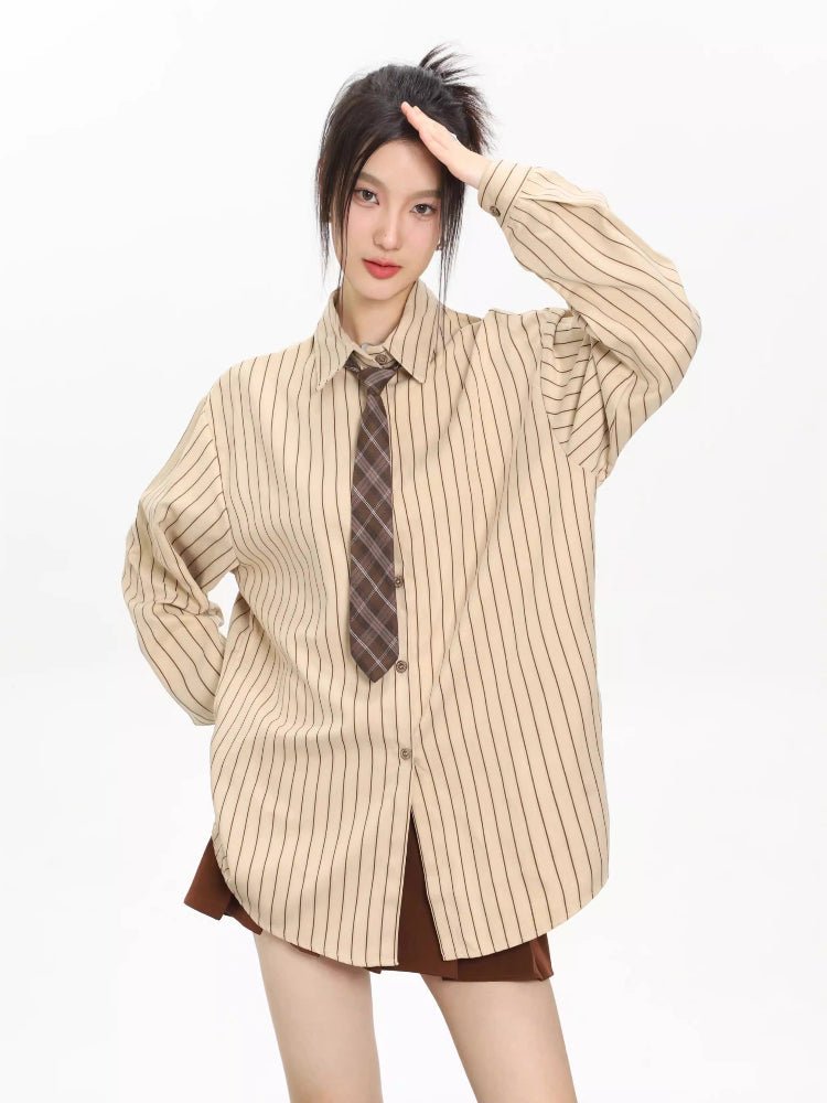 Woman wearing an oversized beige striped button-down shirt with a brown tie, hands on hips.