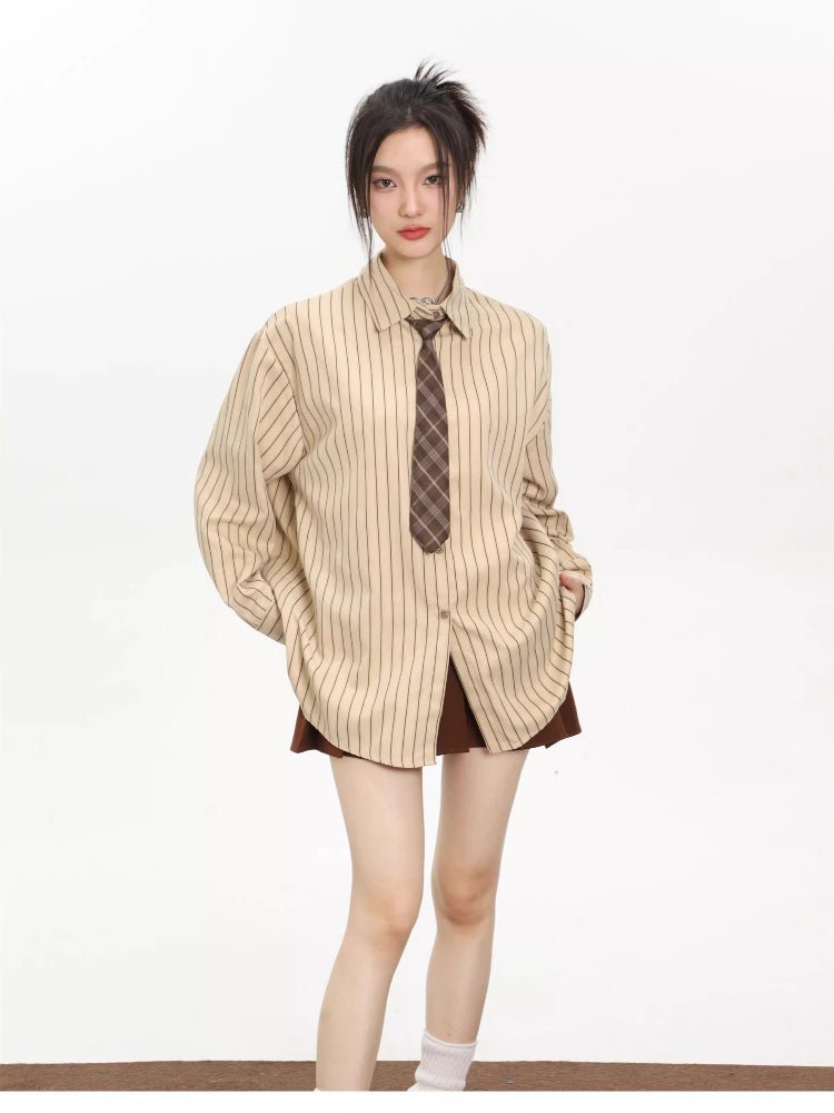 Woman wearing an oversized beige striped button-down shirt with a brown tie, hands in pockets.