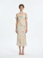 Woman wearing a floral print midi slip dress with off-the-shoulder sleeves and a cowl neckline, standing against a white background.