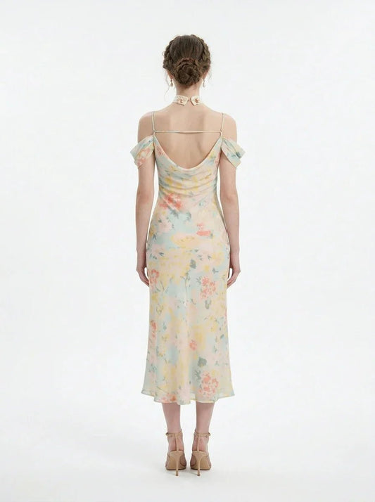 Back view of a woman wearing a floral print midi slip dress with off-the-shoulder sleeves and a cowl neckline, standing against a white background.