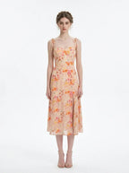 Model wearing a peach floral print midi dress with spaghetti straps and a thigh-high slit, standing against a white background.