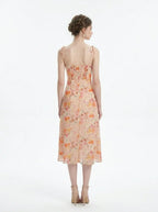 Back view of a peach floral print midi dress with spaghetti straps and a thigh-high slit, standing against a white background.