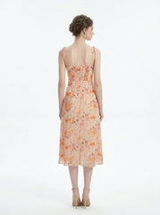 Back view of a peach floral print midi dress with spaghetti straps and a thigh-high slit, standing against a white background.