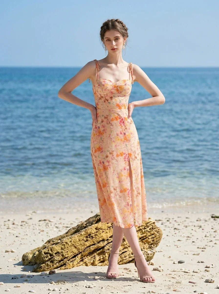 Model wearing a peach floral print midi dress with spaghetti straps and a thigh-high slit, posing on a sandy beach with the ocean in the background.