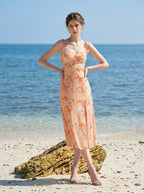 Model wearing a peach floral print midi dress with spaghetti straps and a thigh-high slit, posing on a sandy beach with the ocean in the background.