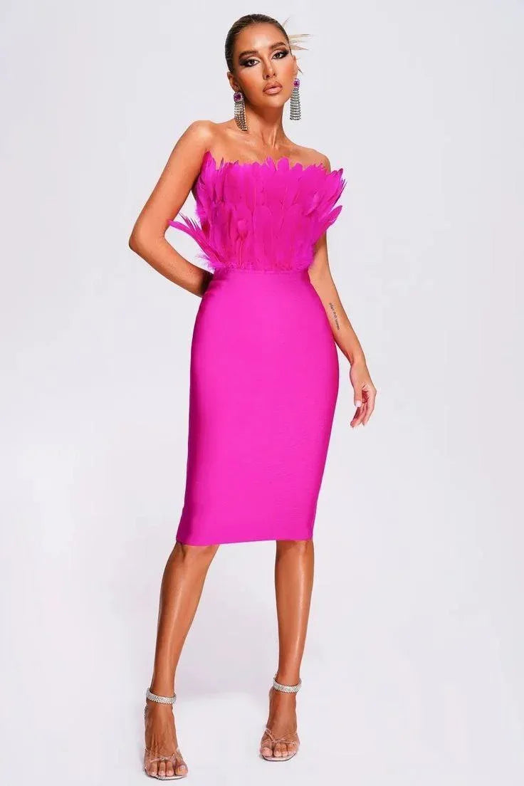 Woman in a hot pink strapless midi dress with a feather-trimmed bodice and statement earrings, posing against a white background.