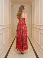 Back view of a woman wearing a red floral print maxi dress with spaghetti straps and a pleated skirt.