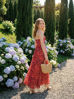 Woman in a red floral print maxi dress holding a straw bag in a garden