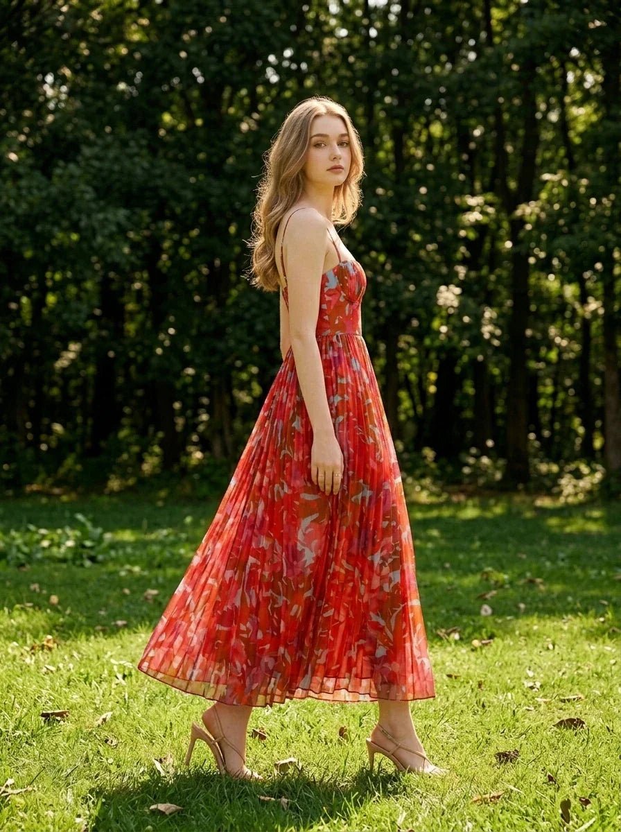Woman walking in a grassy area wearing a red floral print maxi dress with spaghetti straps and a sweetheart neckline.