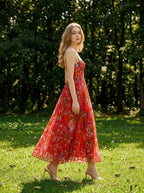 Woman walking in a grassy area wearing a red floral print maxi dress with spaghetti straps and a sweetheart neckline.