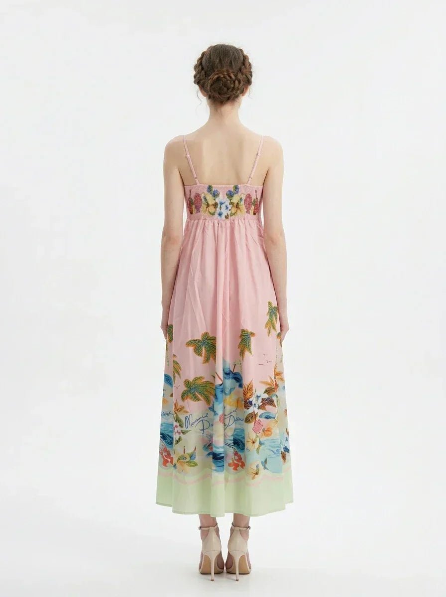 Full back view of a woman wearing a pink midi dress with a tropical print and spaghetti straps, standing against a white background.