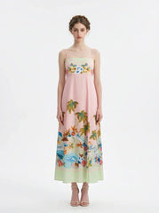 Full front view of a woman wearing a pink midi dress with a tropical print and spaghetti straps, standing against a white background.