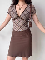 Full body shot of a woman in a plaid top and brown skirt, accessorized with a butterfly necklace.