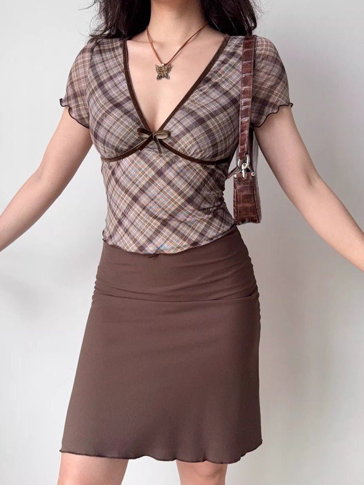 Full body shot of a woman in a plaid top and brown skirt, accessorized with a butterfly necklace.