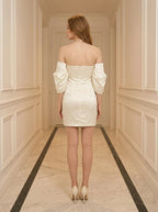 Back view of a woman in a white off-the-shoulder satin mini dress standing in a hallway.