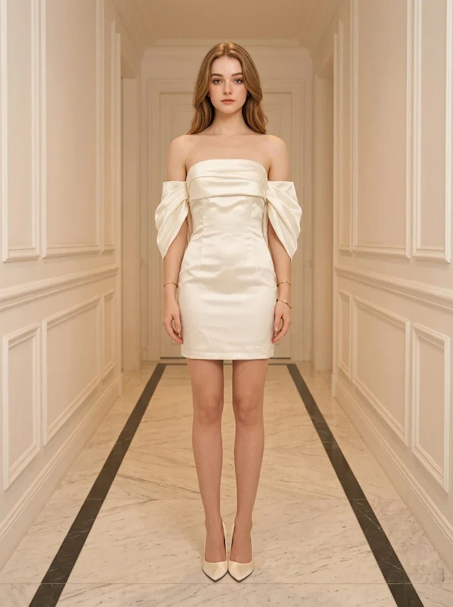 Woman in a white off-the-shoulder satin mini dress standing in a hallway.