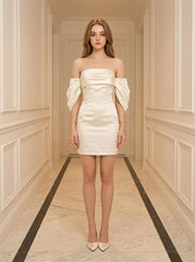 Woman in a white off-the-shoulder satin mini dress standing in a hallway.