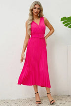 Woman wearing a bright pink sleeveless pleated midi dress with a V-neck and a matching belt