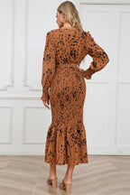 Back view of a woman modeling a long-sleeved, brown and black animal print midi dress with a v-neck, tie waist, and ruffled hem.