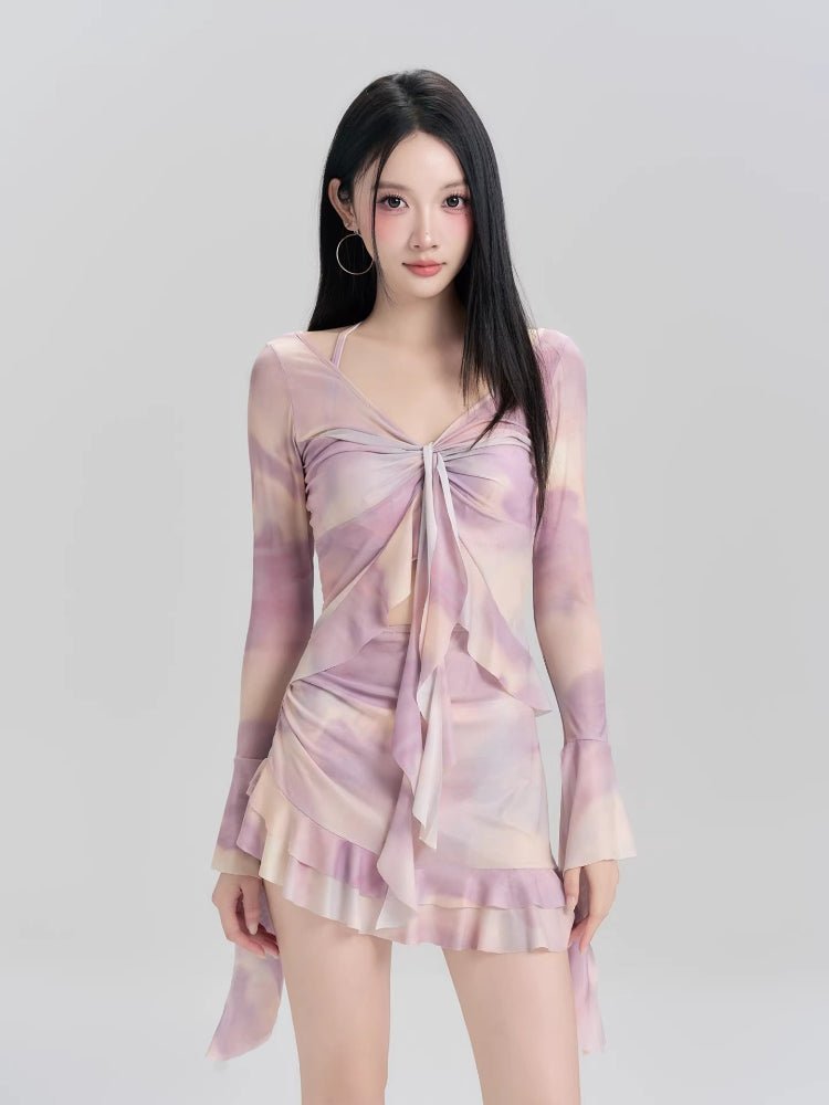 Woman wearing a purple and pink tie-dye mesh cover-up with a tie-front detail and ruffled hem.