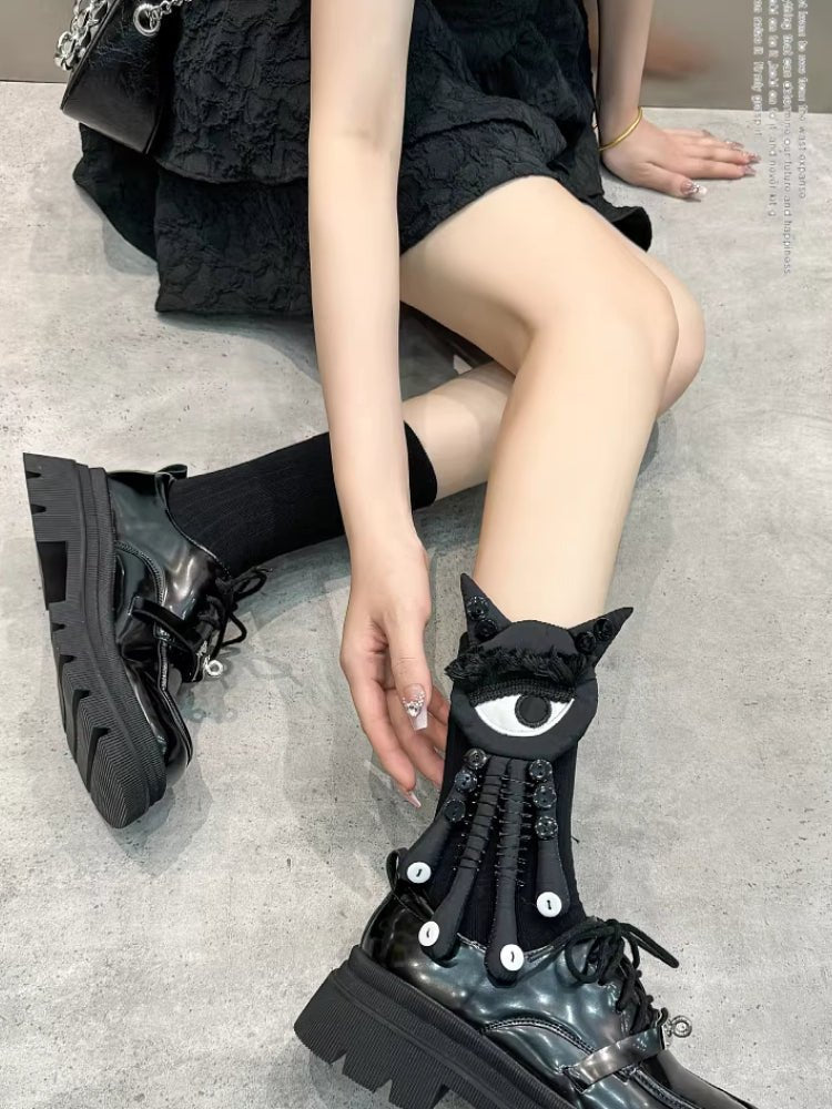 Overhead shot of a person wearing black socks with a black and white eye and tentacle-like attachments, paired with black platform shoes.