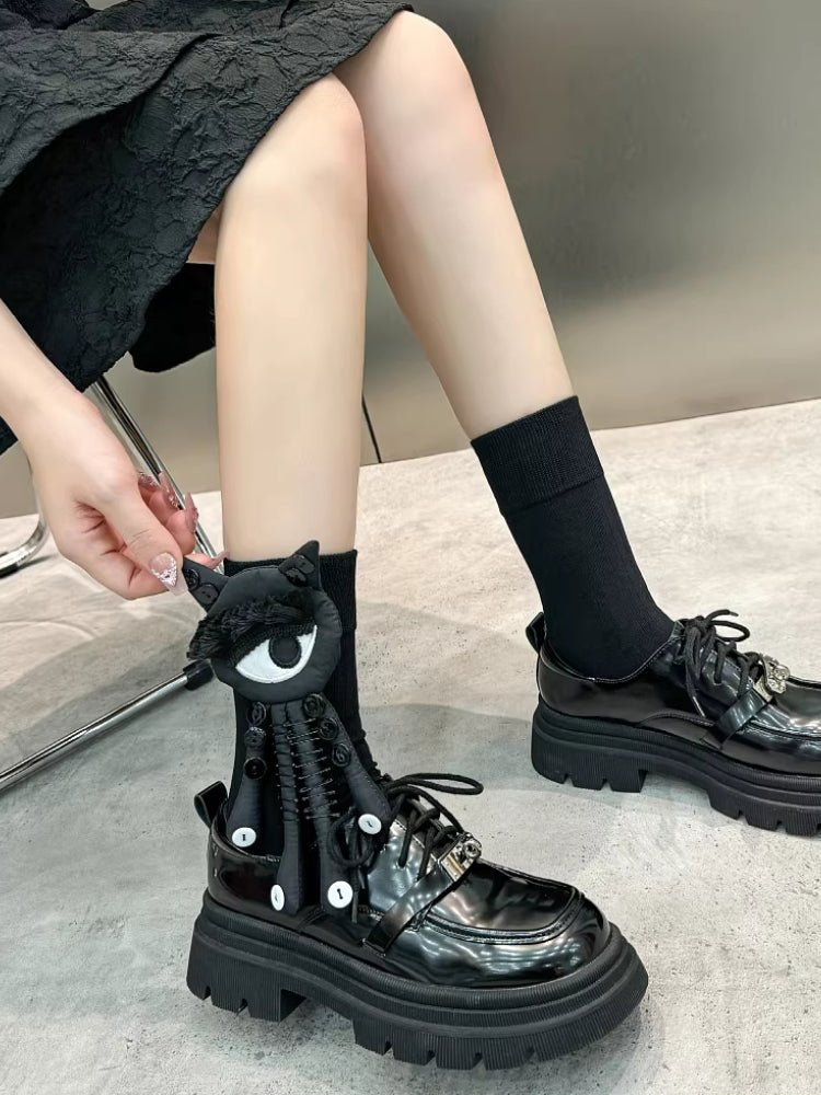 Full view of a person wearing black socks with a black and white eye and tentacle-like attachments, paired with black platform shoes.