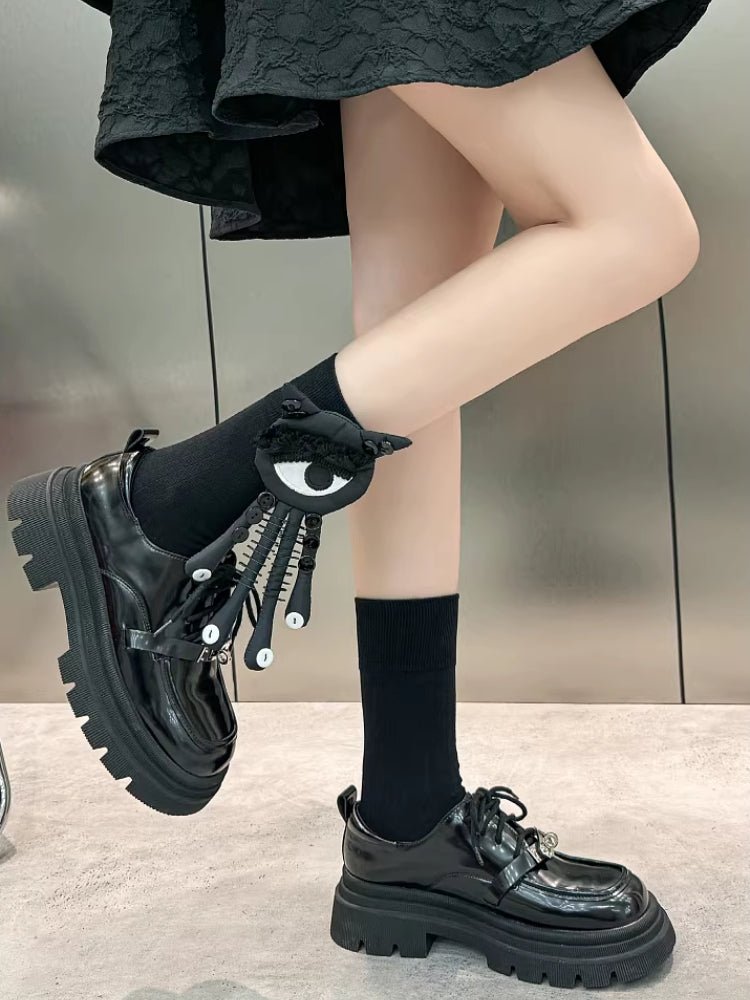 Side view of a person wearing black socks with a black and white eye and tentacle-like attachments, paired with black platform shoes.