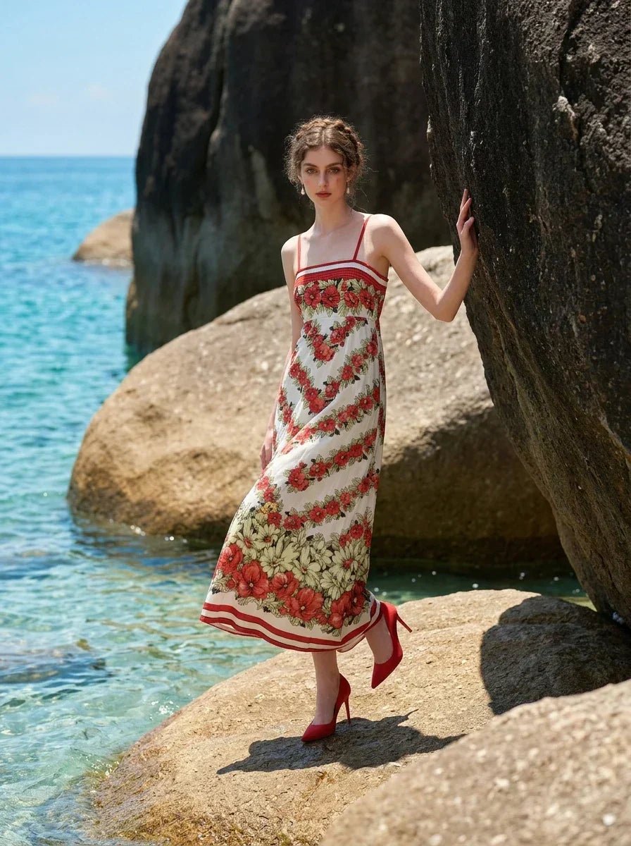 Woman wearing a floral print maxi dress with spaghetti straps, standing on rocks by the sea.