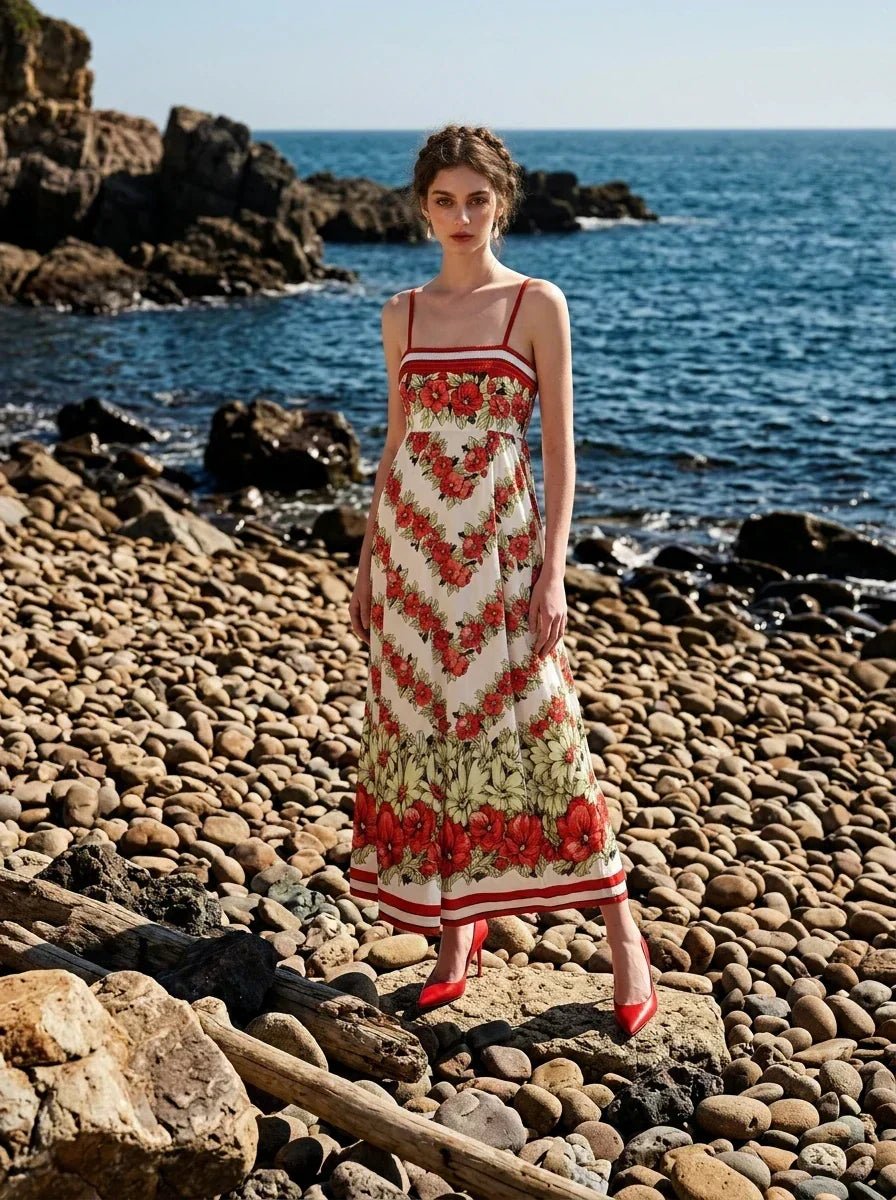 Woman wearing a floral print maxi dress with spaghetti straps, standing on a rocky beach.