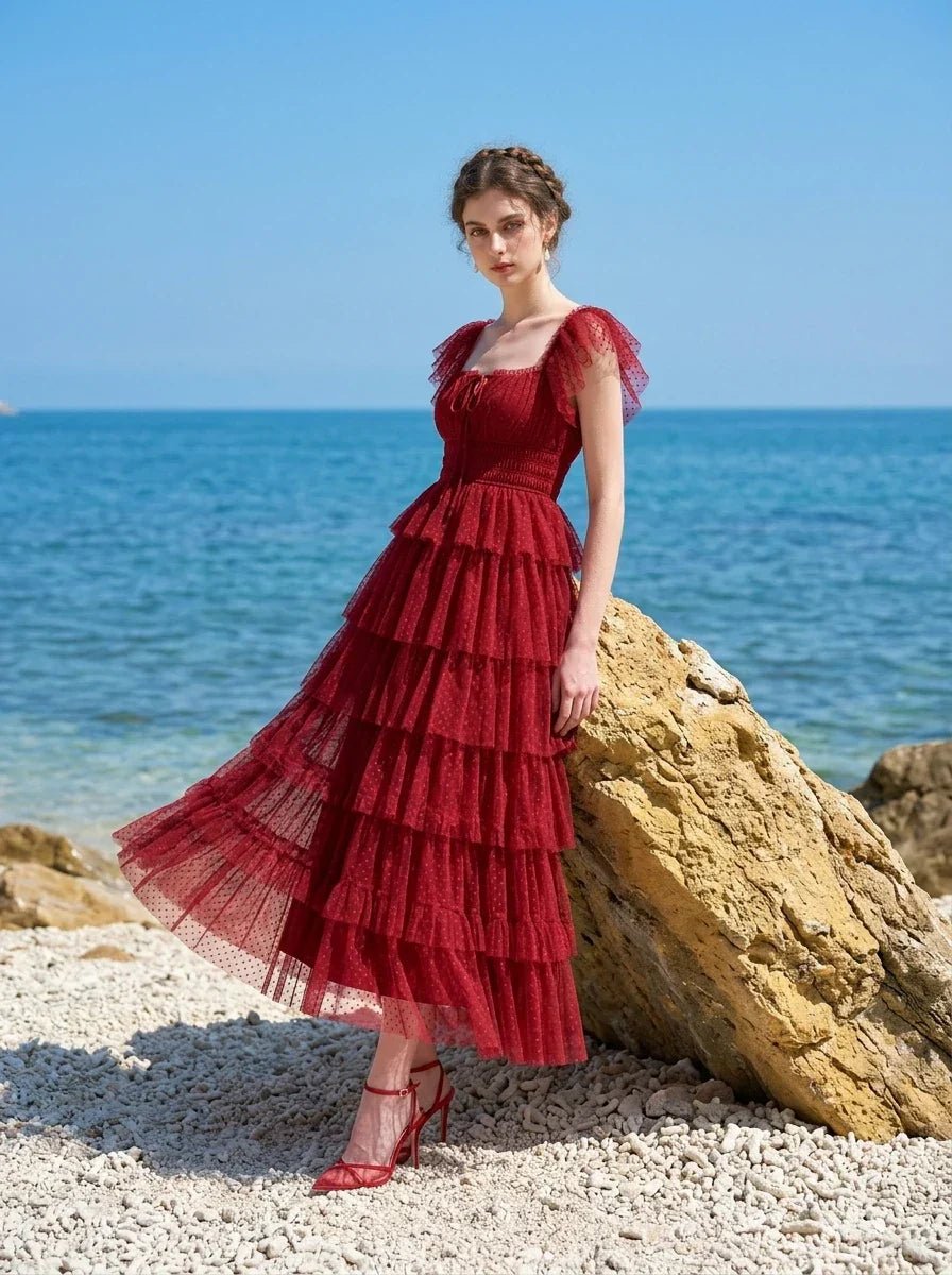 Woman in a red tiered tulle dress with ruffled sleeves and a square neckline, posing on a rock by the sea