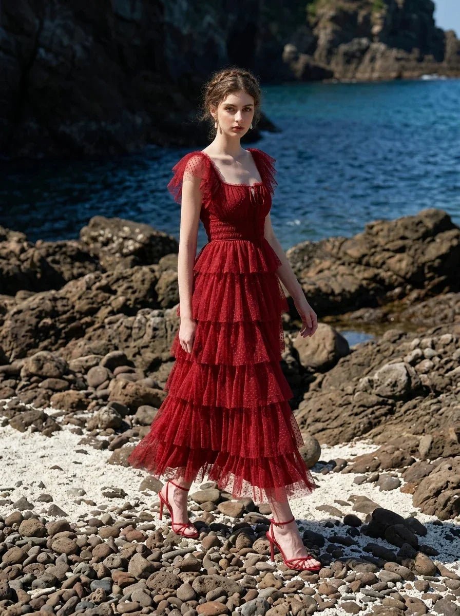Woman in a red tiered tulle dress with ruffled sleeves and a square neckline, walking on a rocky beach