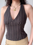 Woman wearing a dark brown halter top with a small floral print and a gold pendant necklace.