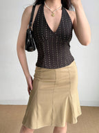 Woman wearing a dark brown halter top, tan skirt, and black handbag.