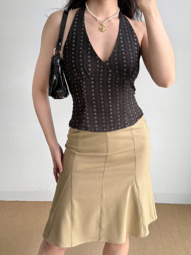 Woman wearing a dark brown halter top, tan skirt, and black handbag.