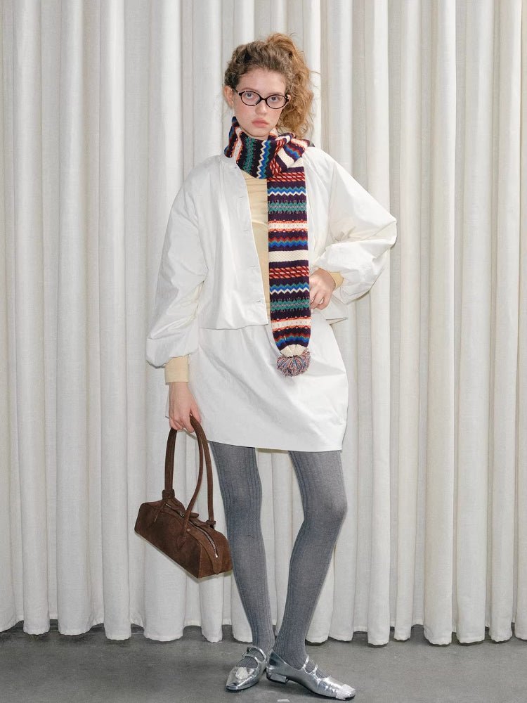 Model posing with a brown handbag, wearing a white jacket, gray tights, silver shoes, and a multicolor knit scarf.