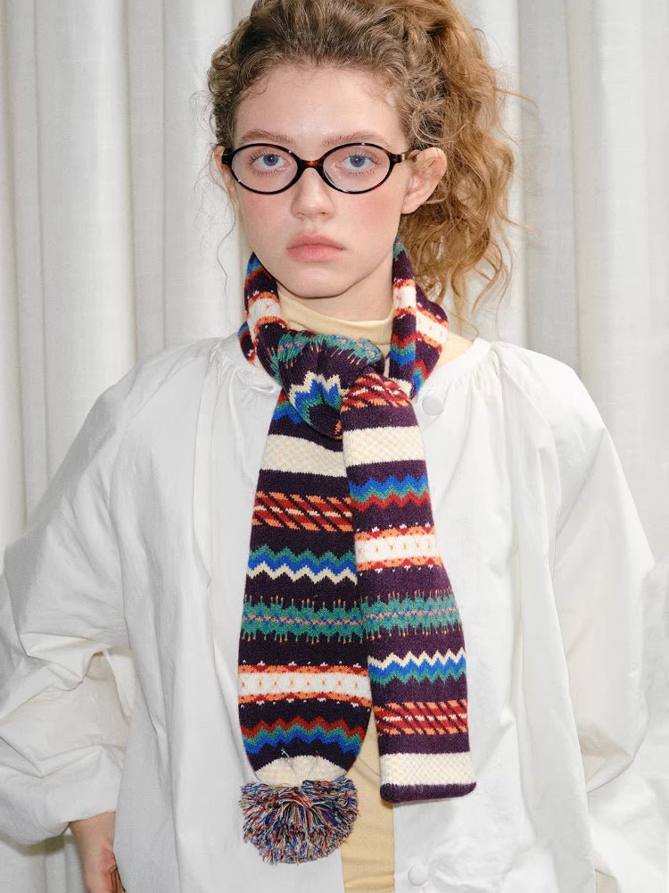 Model wearing a white jacket and a colorful knit scarf with a pom-pom accent.