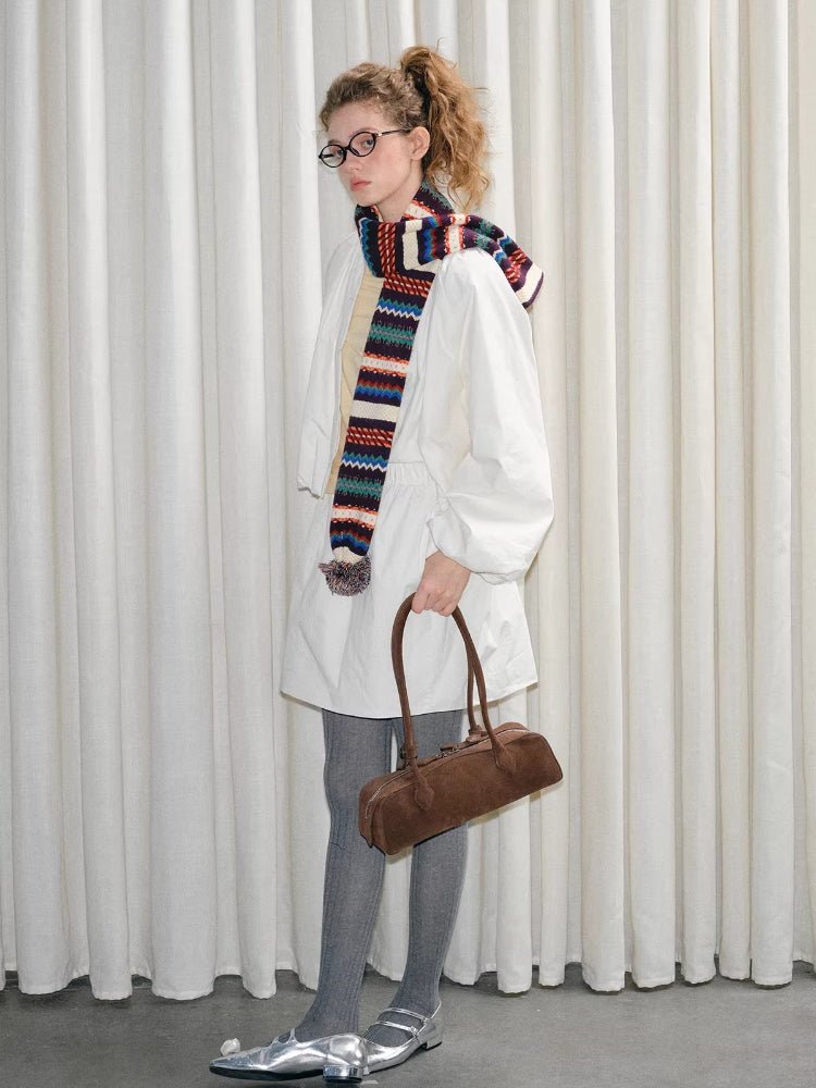 Full body shot of a model wearing a white jacket, gray tights, silver shoes, and holding a brown handbag, with a colorful knit scarf.
