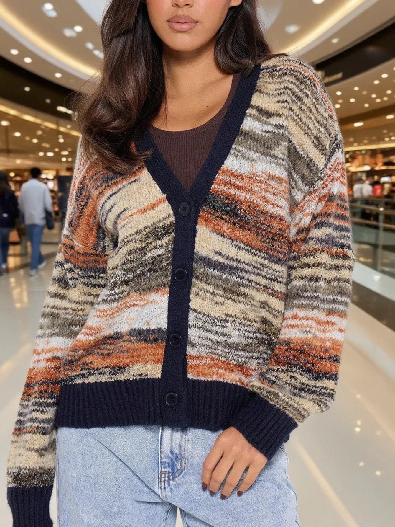 Close-up of a woman wearing a multicolored striped knit cardigan with a V-neck and button-up front, paired with light-wash jeans.